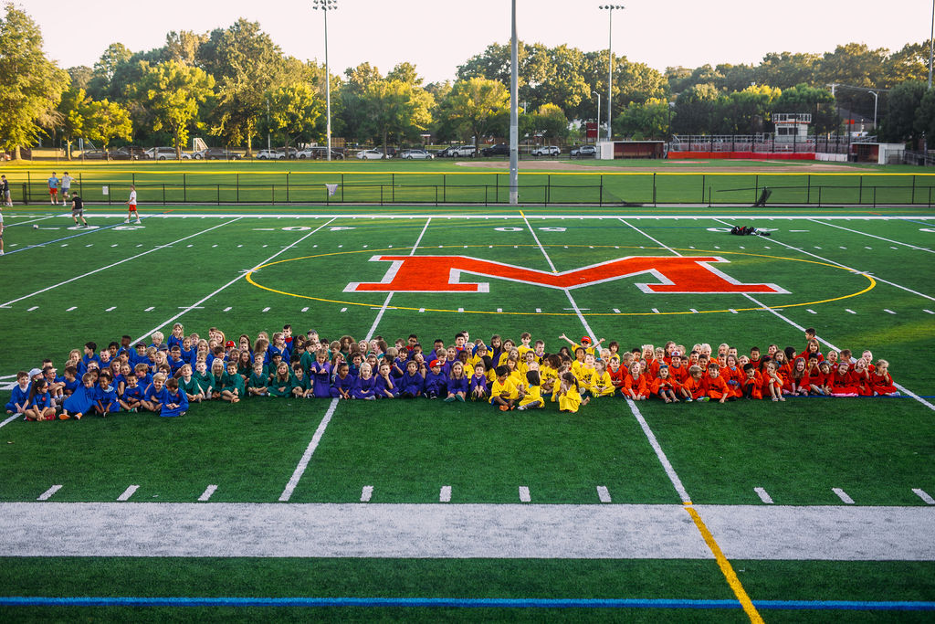 children sitting on football field in colorful t-shirts