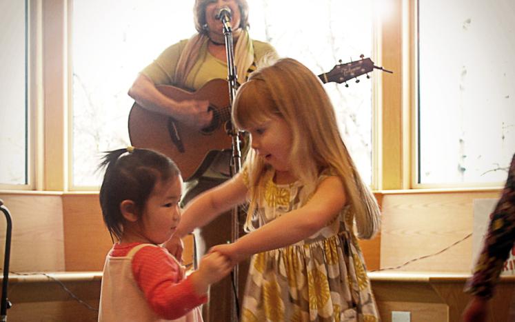 Photo of Jeannie Mack playing guitar and two children dancing